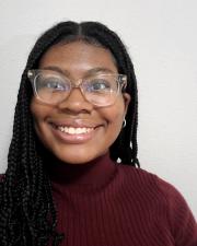 Andrea stands in front of a blank background wearing a maroon sweater and smiling. 